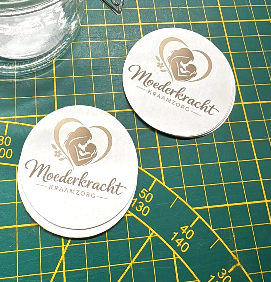 Ronde stickers met het logo van Moederkracht Kraamzorg naast een glazen pot
